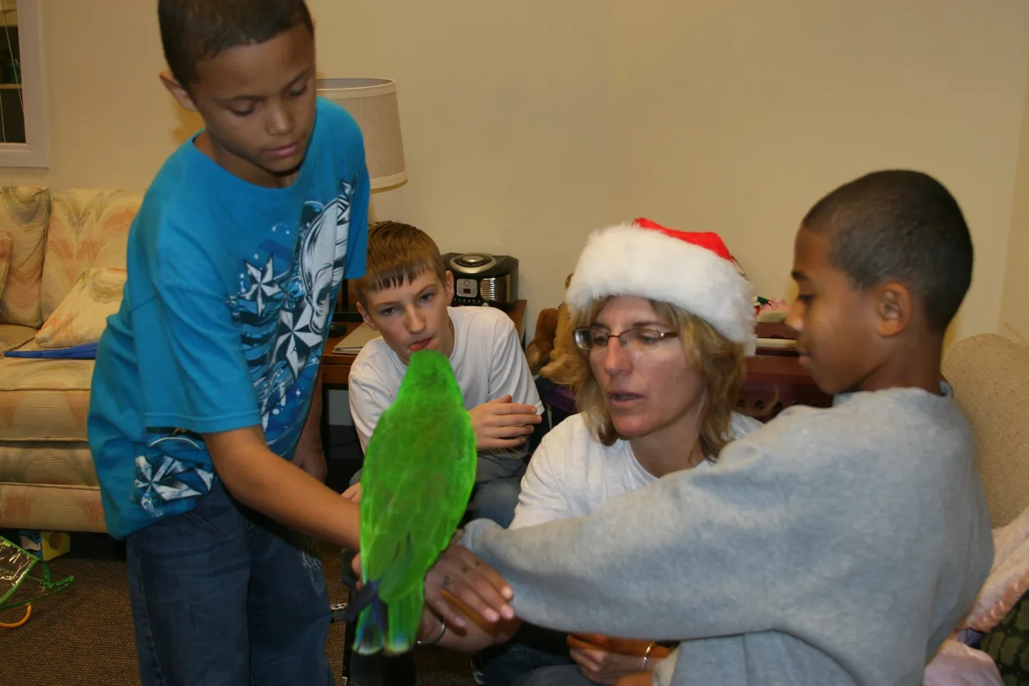 A woman holding a parrot in her hand while two boys watch.